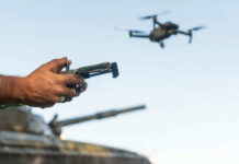 Person controlling a drone with a remote while a tank is in the background