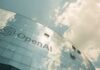 A modern glass building with the OpenAI logo against a cloudy sky