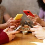 Group of friends sitting at a table, each using their smartphones