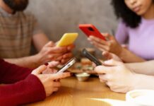 Group of friends sitting at a table, each using their smartphones