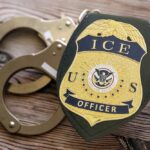 ICE officer badge next to handcuffs on a wooden surface