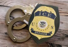 ICE officer badge next to handcuffs on a wooden surface