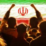 Crowd of people raising their fists in front of the Iranian flag