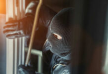 A masked individual attempting to break into a building with a crowbar
