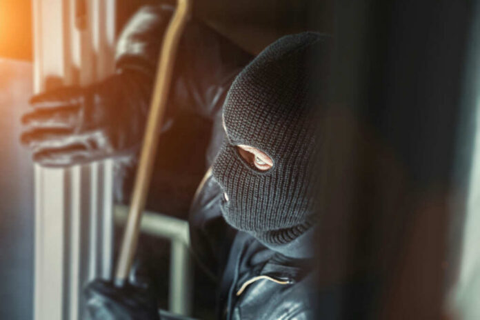 A masked individual attempting to break into a building with a crowbar