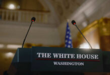 Press podium with microphones and an American flag in the background