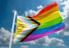 Faith Versus Mandate: Pride Flag Battle Hits Federal Court A colorful pride flag waving against a blue sky with clouds