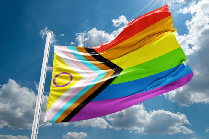 A colorful pride flag waving against a blue sky with clouds
