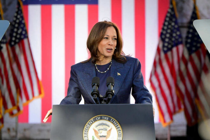 A female political leader speaking at a podium with American flags in the background