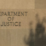 Sign reading Department of Justice on a stone wall with a shadow