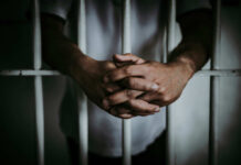 Domestic Violence Charge: NFL Star in Jail A close-up of a persons hands clasped together in front of prison bars