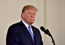 Trump Iran Clash Hijacks Memorial Day A political figure standing at a microphone with a serious expression