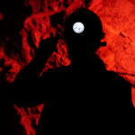 Silhouette of a miner wearing a headlamp against a red rocky background