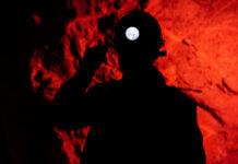 Laos Cave Rescue GRIPS World: Surviving the Unimaginable! Silhouette of a miner wearing a headlamp against a red rocky background