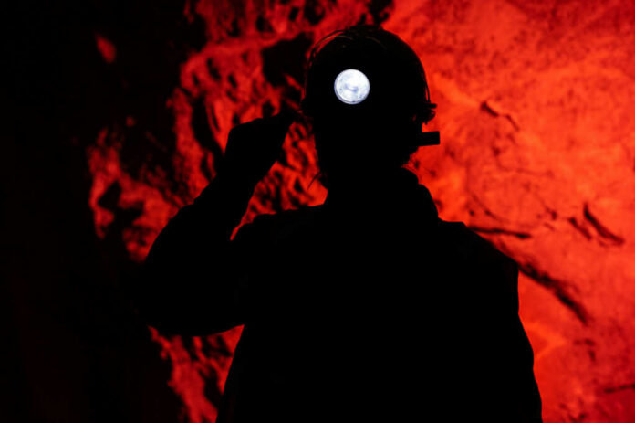 Silhouette of a miner wearing a headlamp against a red rocky background