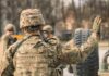 A soldier in camouflage uniform saluting with one hand raised