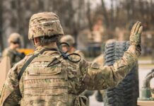 A soldier in camouflage uniform saluting with one hand raised