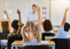 NYC School Simulation Sparks Outrage at Big Tech Children in a classroom raising their hands to answer a question while a teacher stands in front