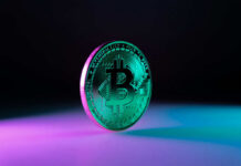 Treasury Freezes Iran’s Digital War Chest A shiny Bitcoin coin illuminated with colorful lighting against a dark background