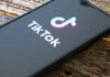 Germany’s TikTok Seizure Bid: Shocking Precedent Close-up of a smartphone displaying the TikTok logo on a wooden surface