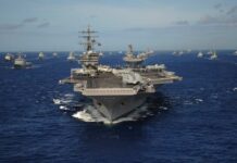 An aircraft carrier surrounded by various naval ships in the ocean