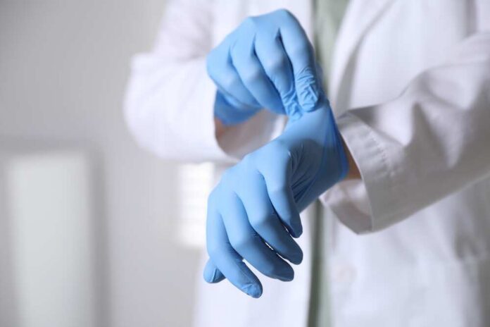 Medical,Worker,Putting,On,Gloves,In,Hospital,,Closeup A medical professional putting on blue gloves in a clinical setting