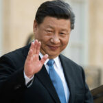 A political leader in formal attire smiling and waving