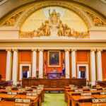 Interior view of a legislative chamber with wooden furniture and decorative ceiling