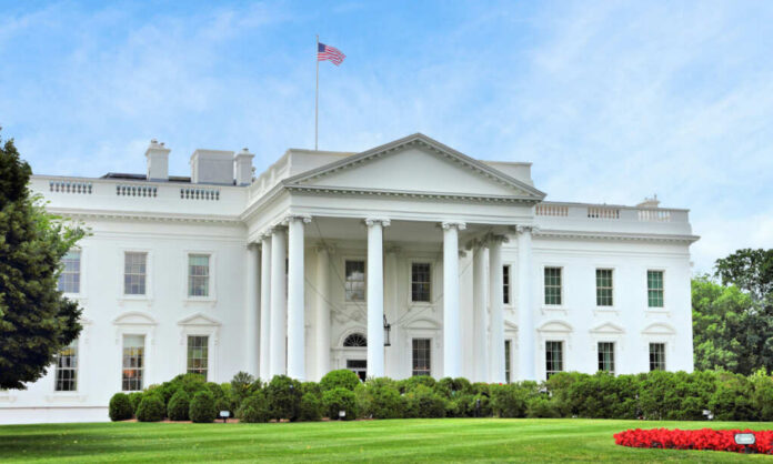 shutterstock2502569527jpg The White House with an American flag flying above, surrounded by greenery