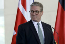 Face Scan Britain? Starmer’s Next Move A man in formal attire standing at a podium with flags in the background
