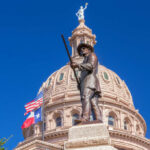 Bible Mandate Ignites Texas Firestorm Bronze statue in front of the Texas State Capitol building under a clear blue sky