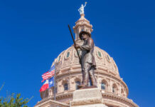 Bronze statue in front of the Texas State Capitol building under a clear blue sky