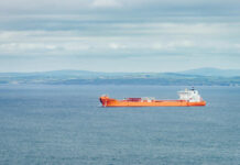 An orange cargo ship sailing in the ocean with a coastal landscape in the background