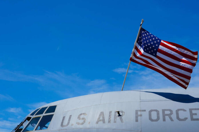 shutterstock_2159722029 Close-up of a U.S. Air Force aircraft with an American flag waving against a blue sky