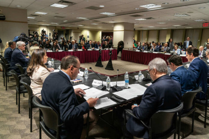 A formal government meeting with officials seated around a table and media present
