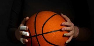 Hands with bandages holding an orange basketball against a dark background