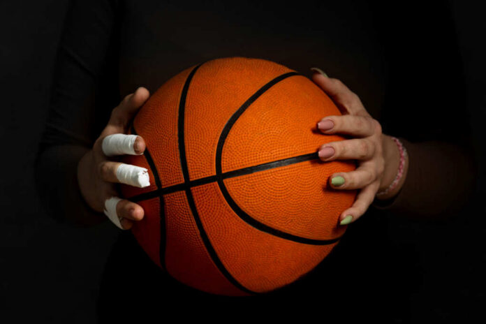 Hands with bandages holding an orange basketball against a dark background