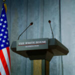 Press podium with microphones and American flag in the background