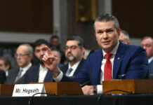 Hegseth Drops NATO Bombshell Review A man in a blue suit speaking at a senate hearing with a panel of officials behind him
