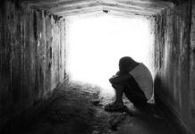 3,000-Foot Cartel Tunnel Stuns San Diego A person sitting in a dark tunnel, hugging their knees with light visible at the end