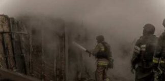 Firefighters spray water into a smoke-filled structure
