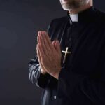 Extremist Tag Backfires — Chaplain Vindicated Clergyman in black robe praying with hands together