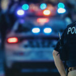 Birmingham Arrest Lights Policing Firestorm Police officer in a tactical vest standing in front of a police car with flashing lights