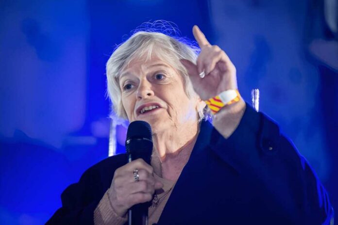 shutterstock_1632176155-1 Older woman speaking with microphone, hand raised
