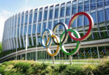 Olympic U-Turn Throws LA 2028 Into Chaos Colorful Olympic rings displayed in front of a modern building