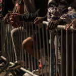 July 4 Flashpoint: Teen Takeovers Loom Close-up of hands resting on a barrier in a crowded urban setting