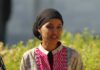 A woman in traditional attire smiling outdoors with greenery in the background