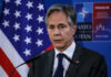 A government official speaking at a press conference with a flag in the background