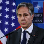 €70 Billion Mirage? NATO Math Unravels A government official speaking at a press conference with a flag in the background