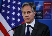 €70 Billion Mirage? NATO Math Unravels A government official speaking at a press conference with a flag in the background